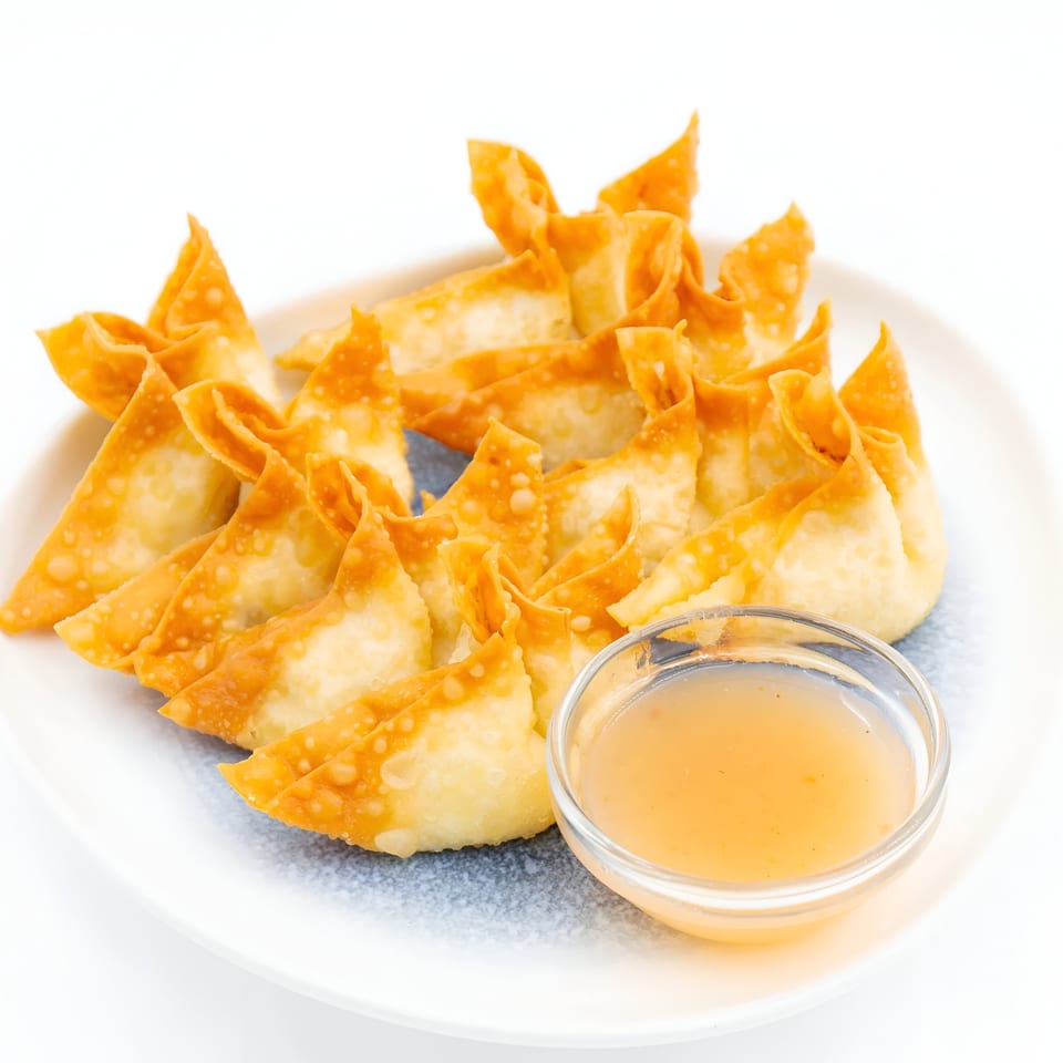 Golden-fried crab rangoons with a side of sweet and sour dipping sauce on a white plate.