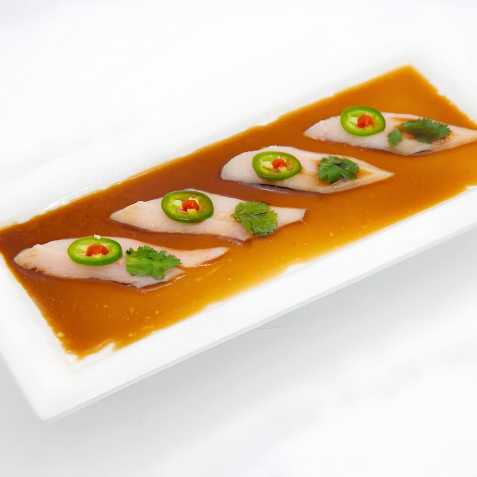 Four pieces of Jade Lowell's Asian-fusion sashimi, garnished with jalapeño and cilantro, in a savory sauce.