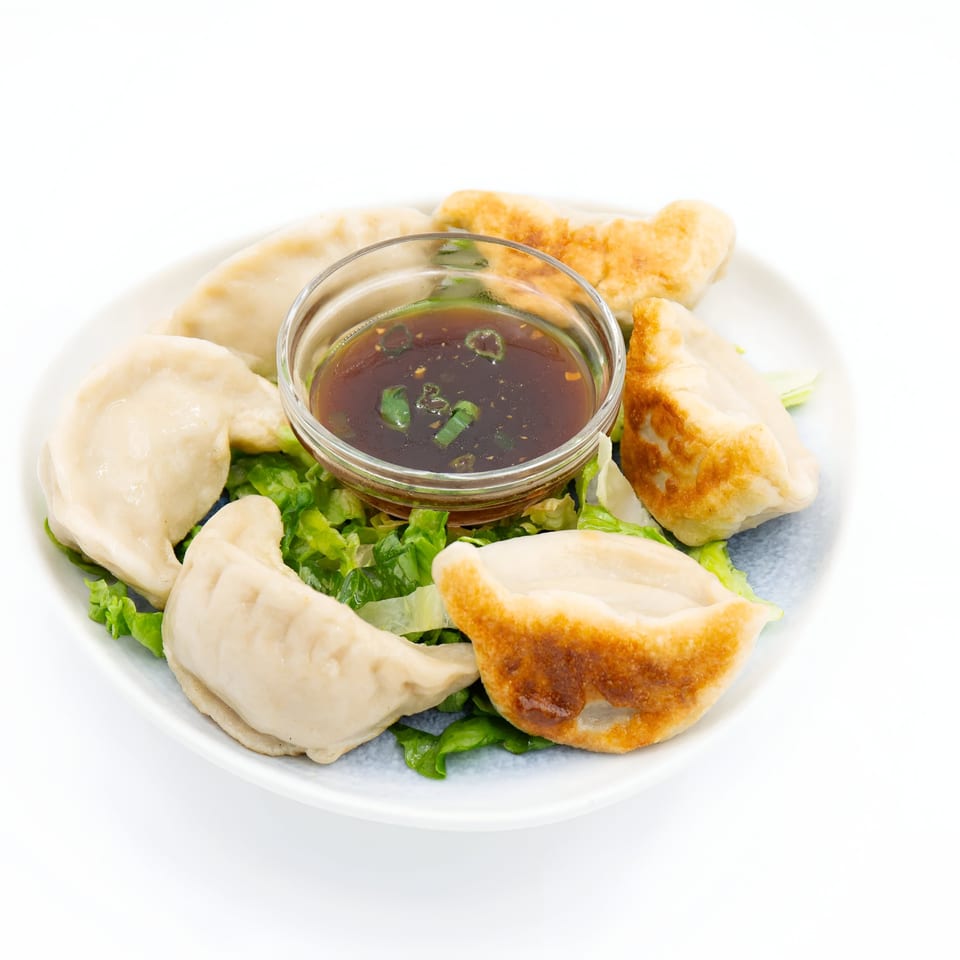 A plate of Jade Lowell's pan-fried and steamed dumplings with a side of dipping sauce.